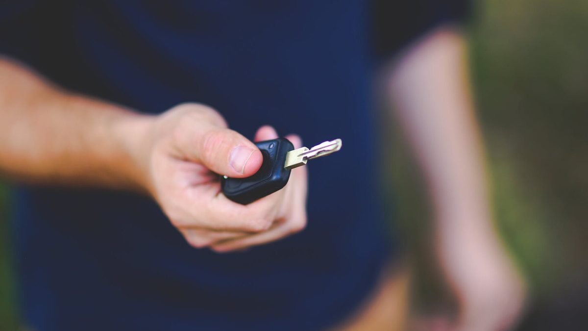 Ausgestreckte Hand übergibt einen Autoschlüssel vor unscharfem Hintergrund