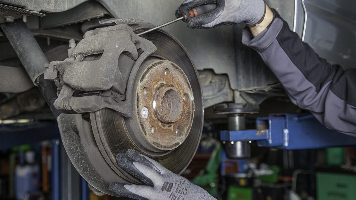 Mechaniker mit Arbeitshandschuhen prüft die Bremsscheibe eines Autos auf der Hebebühne
