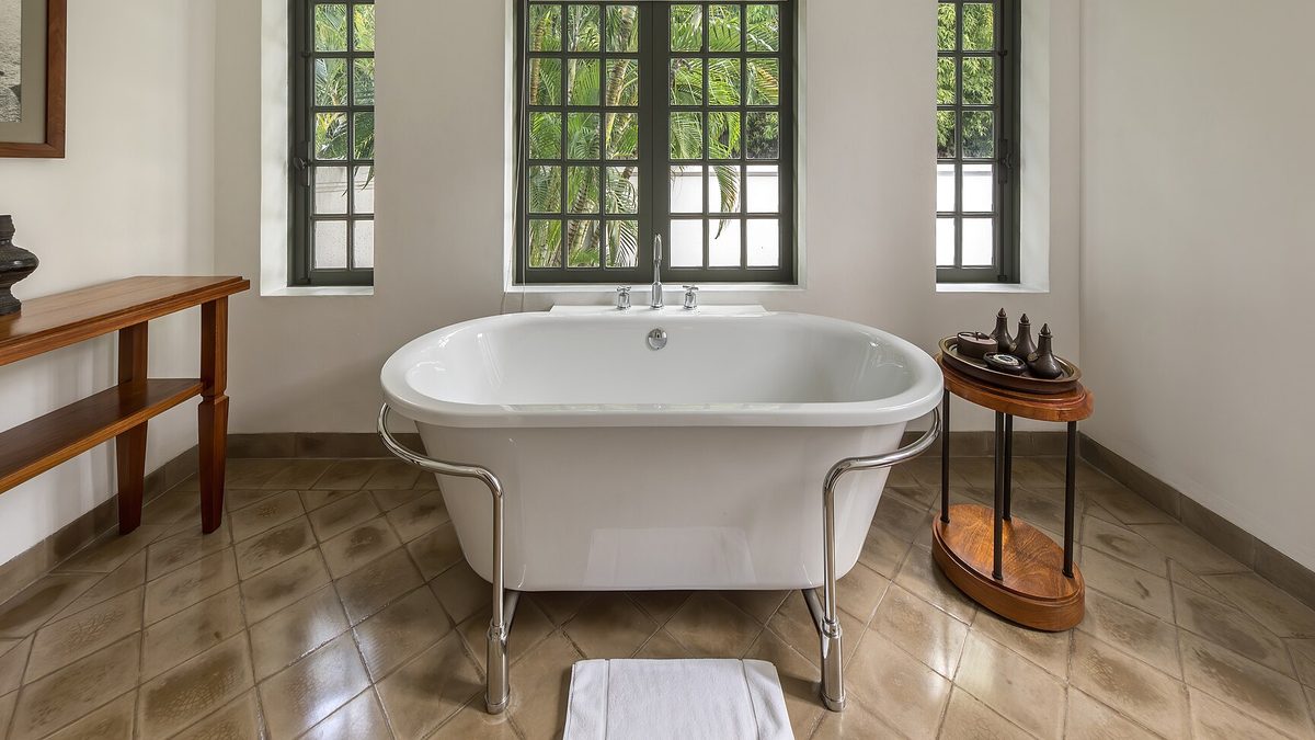 Freistehende weiße Badewanne vor hohen Sprossenfenstern in einem hellen Badezimmer