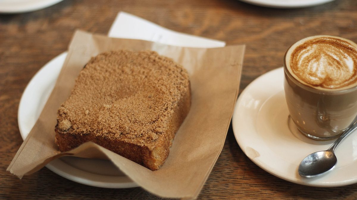 Stück Kuchen und Cappuccino mit Milchschaum-Muster auf einem Holztisch im Café