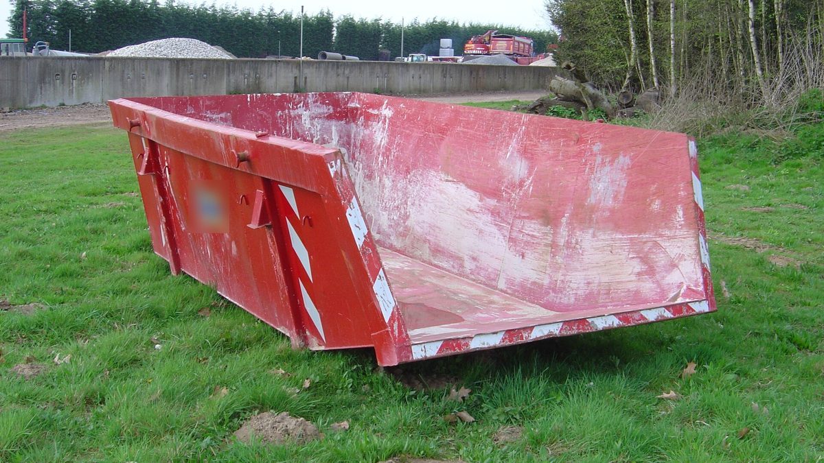 Leerer roter Absetzcontainer für Bauschutt auf einer grünen Wiese