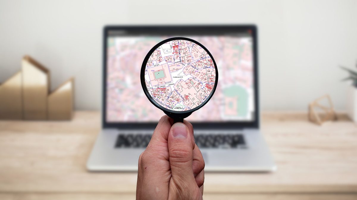Hand hält eine Lupe vor einen Laptop mit einem detaillierten Stadtplan