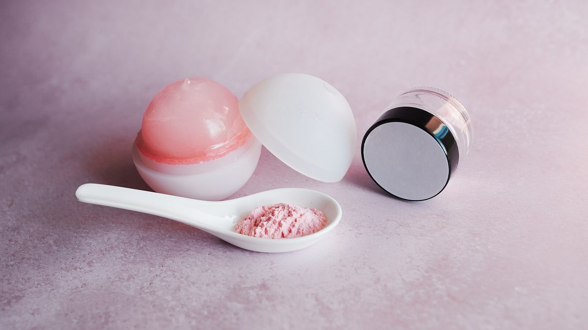 Pflegeprodukte mit Lippenbalsam, Cremedose und rosa Puder auf einem weißen Löffel
