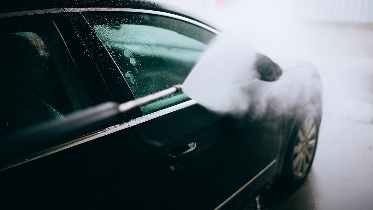 Hochdruckreiniger sprüht Wasser auf die Seite eines dunklen Autos