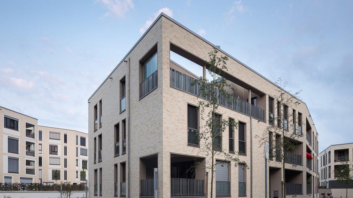 Modernes Mehrfamilienhaus mit heller Klinkerfassade, Balkonen und jungen Bäumen