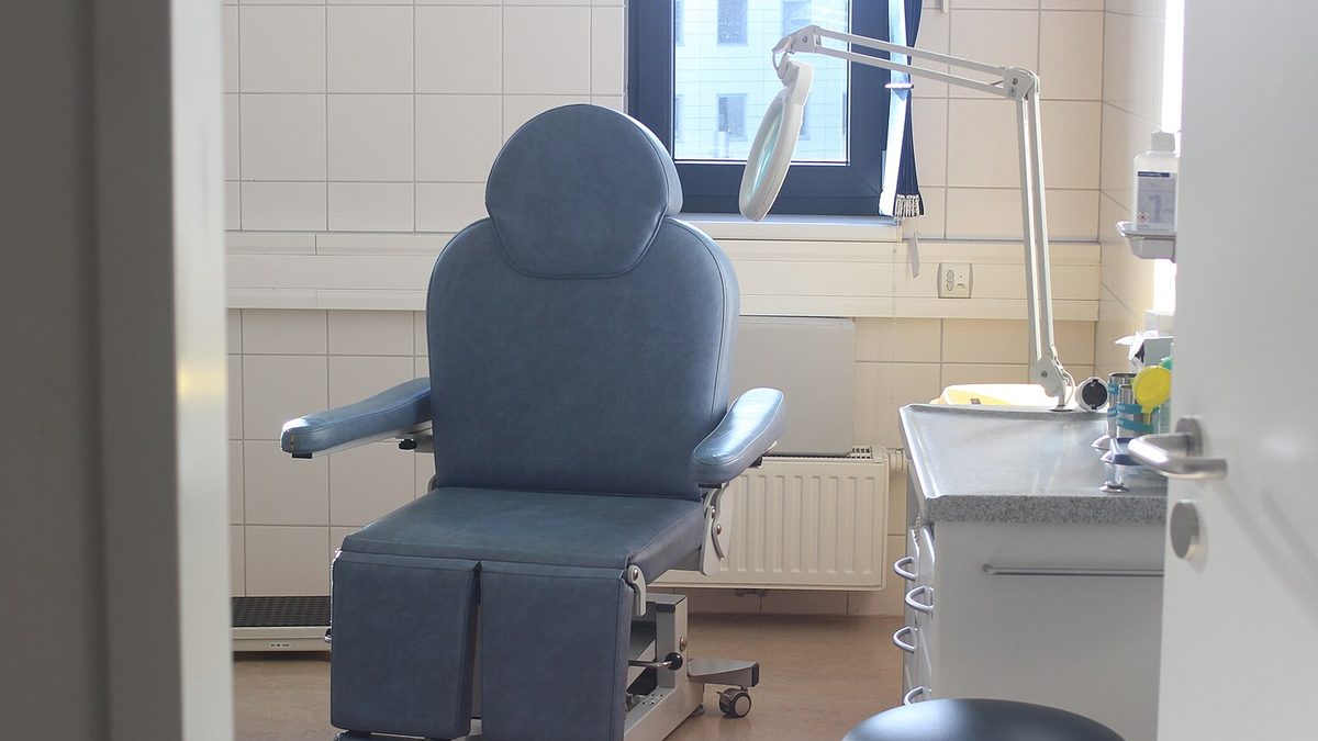 Leerer heller Behandlungsraum mit blauem Behandlungsstuhl, Lupenleuchte und Arbeitsschrank