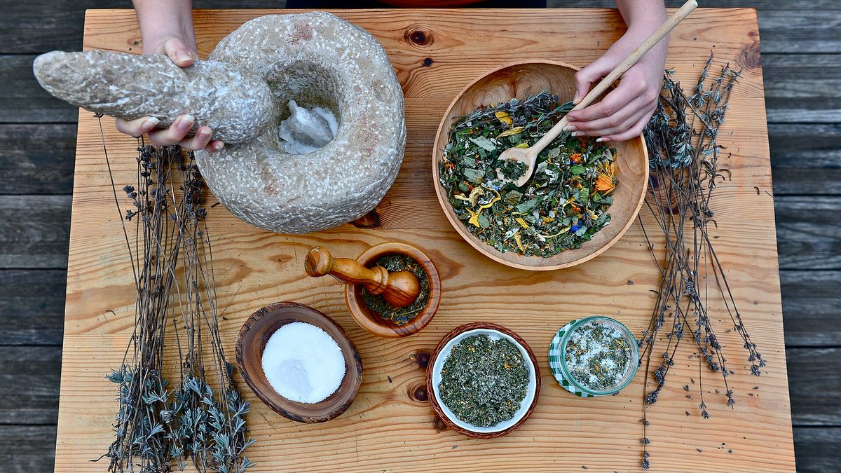 Getrocknete Heilkräuter, Lavendelbündel und Steinmörser auf einem hellen Holztisch