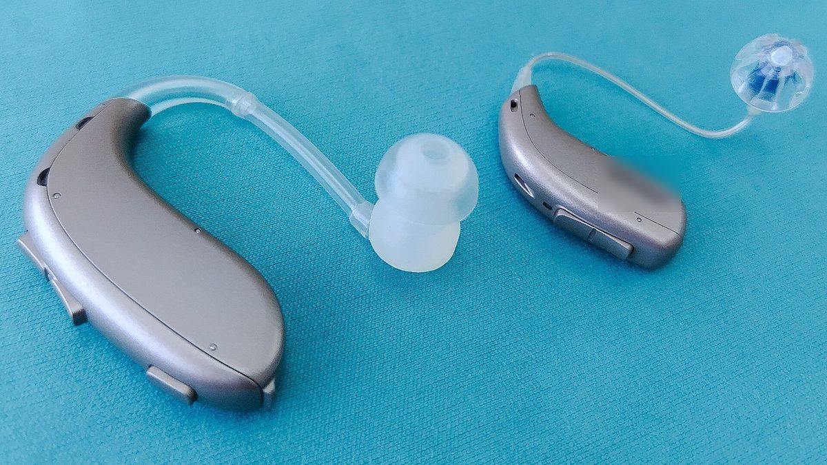 Zwei moderne Hinter-dem-Ohr-Hörgeräte auf türkisfarbenem Stoff als neutrale Produktaufnahme