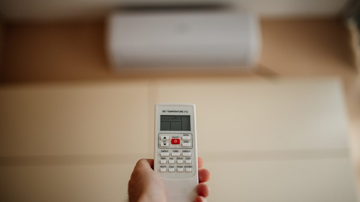 Hand richtet eine Fernbedienung auf ein Klimagerät an der Wand