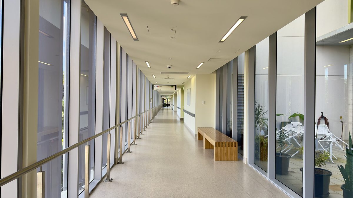 Heller, leerer Krankenhausflur mit Glasfront, Handlauf und Holzbank
