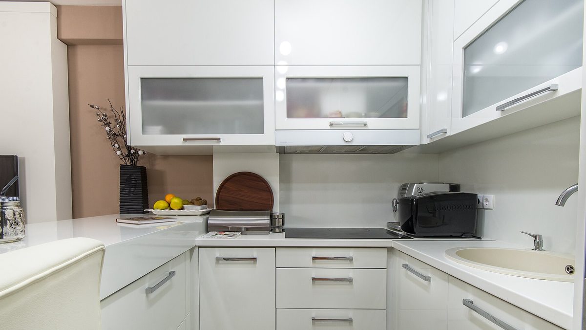 Moderne weiße Einbauküche mit Hochglanzfronten, Glas-Oberschränken und heller Arbeitsplatte