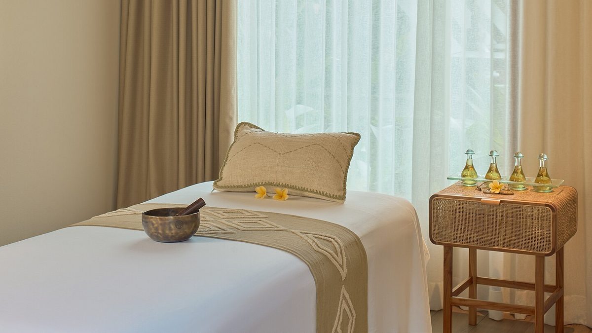 Massageliege mit weißem Laken, Kissen, Klangschale und Fläschchen mit Massageöl