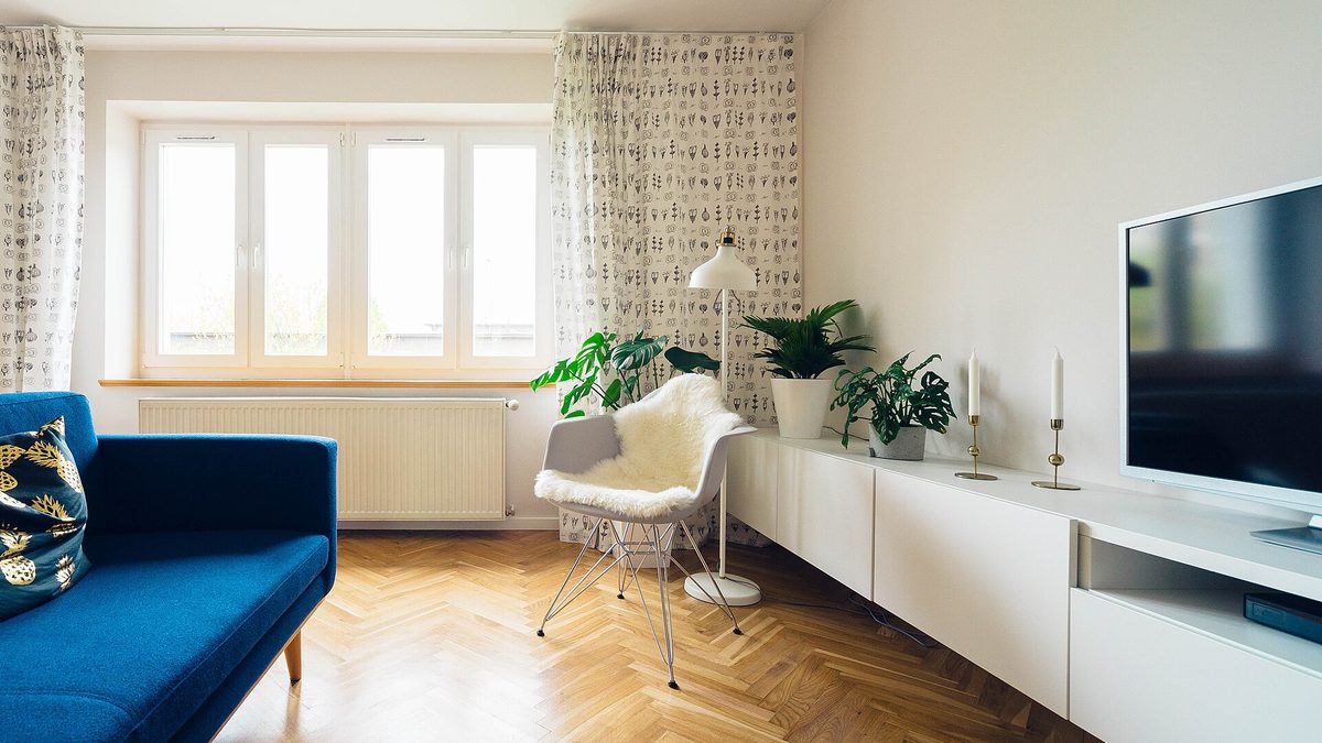 Helles Wohnzimmer mit blauem Sofa, weißem Sideboard, Sessel und Zimmerpflanzen