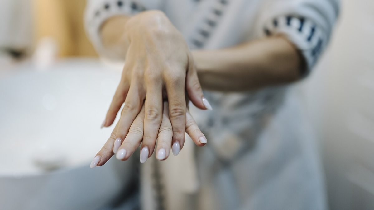 Gepflegte Hände mit hellrosa lackierten, mandelförmigen Fingernägeln vor hellem Hintergrund