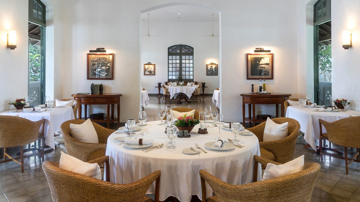 Heller Speisesaal eines Restaurants mit weiß gedeckten runden Tischen und Korbsesseln