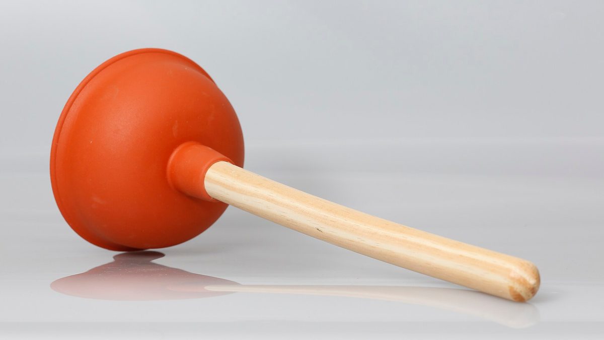 Saugglocke mit orangefarbenem Gummikopf und Holzstiel auf hellem Untergrund