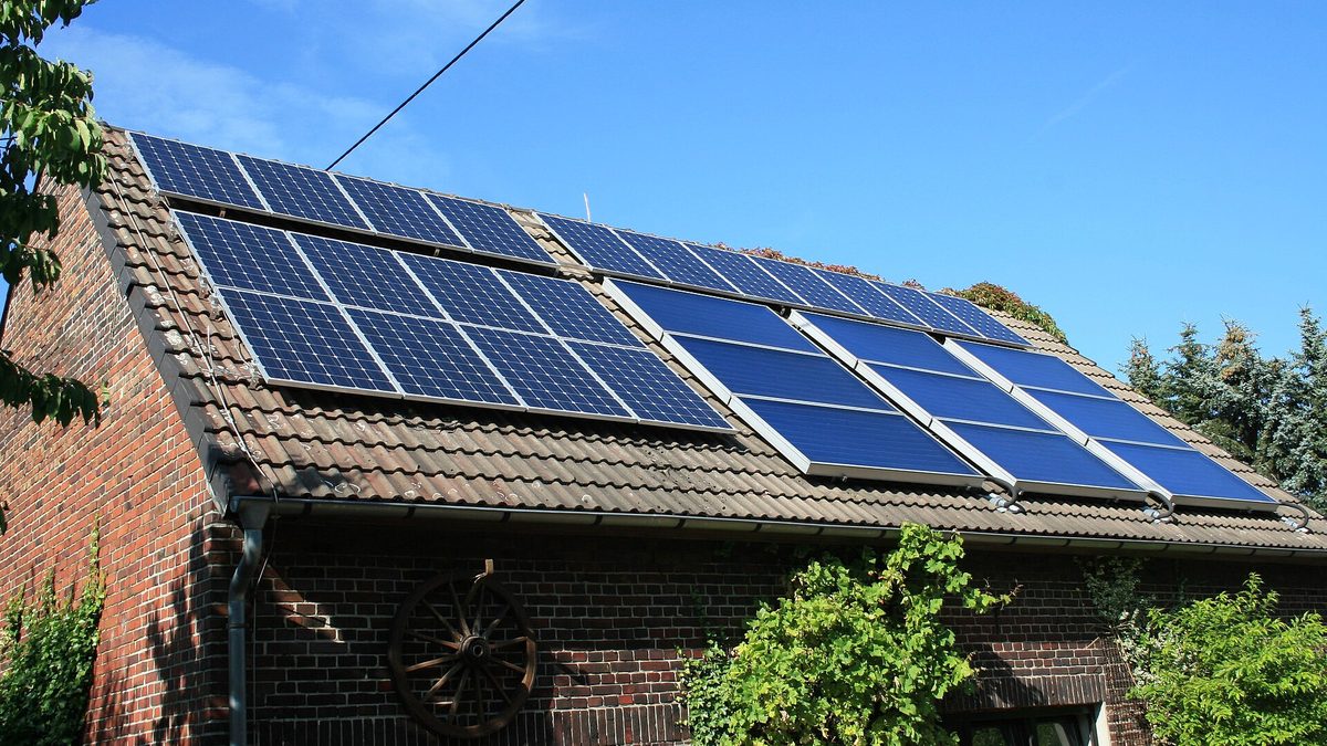 Photovoltaik- und Solarthermie-Module auf dem Ziegeldach einer Backsteinscheune unter blauem Himmel