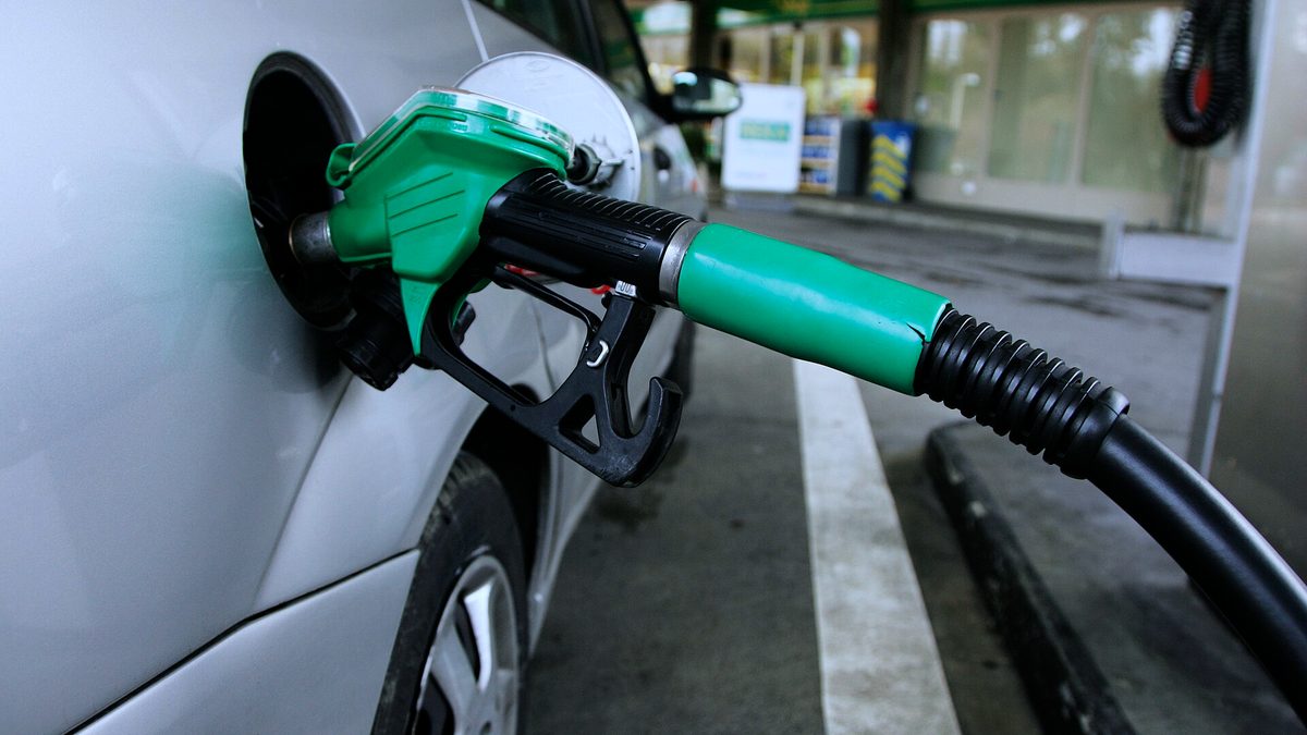 Grüne Zapfpistole steckt im Tankstutzen eines silbernen Autos an der Tankstelle