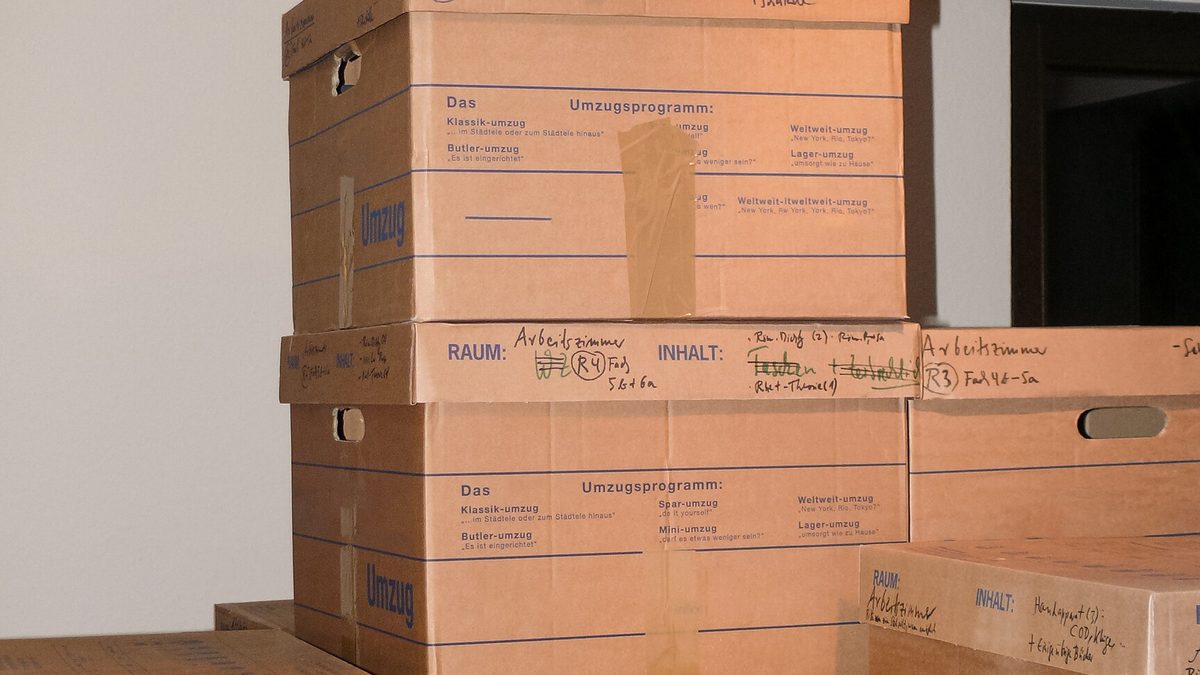 Gestapelte Umzugskartons mit handschriftlicher Beschriftung von Raum und Inhalt